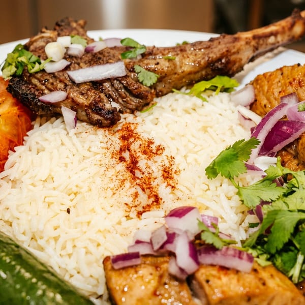 Grilled lamb chop and chicken skewers with rice, roasted tomato, cucumber, and red onion.
