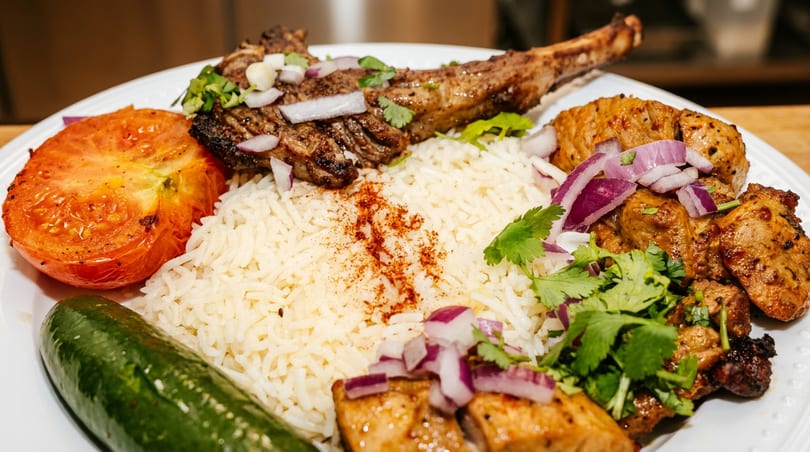 Grilled lamb chop and chicken skewers with rice, roasted tomato, cucumber, and red onion.