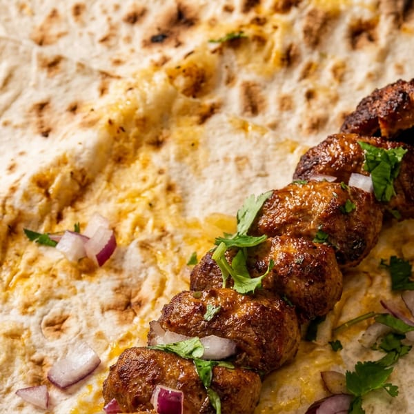 Grilled meat skewer with fresh cilantro and red onions on a flatbread.