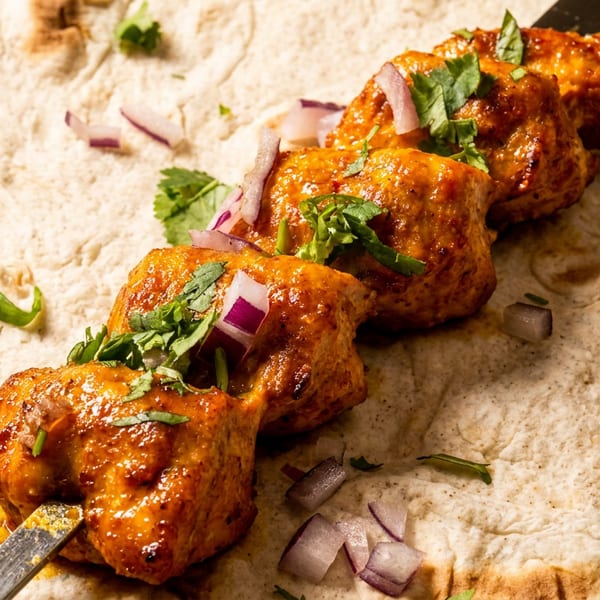 Chicken tikka skewers with cilantro and red onions on a flatbread.