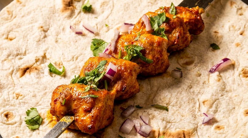 Chicken tikka skewers with cilantro and red onions on a flatbread.