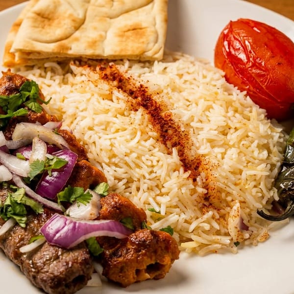 A plate of koobideh and chicken shish kebabs with rice, grilled tomato, jalapeño, and naan.