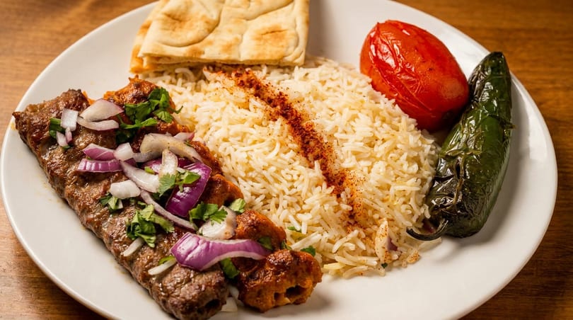 A plate of koobideh and chicken shish kebabs with rice, grilled tomato, jalapeño, and naan.